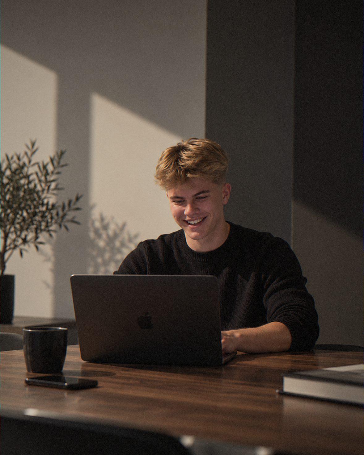 Albert Nørhave sidder ved et bord med sin bærbare computer og smiler i eftermiddagssollys.